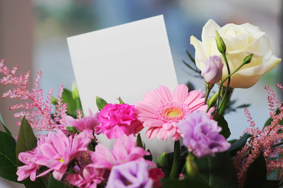 A vibrant floral arrangement featuring a white rose, pink gerbera daisies, purple eustoma, and pink astilbe, accented with green foliage. The flowers are freshly cut with visible petals, arranged in a